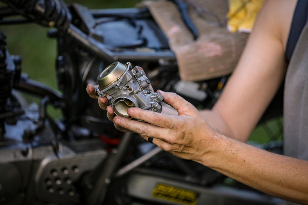 Close-up of hands holding a motorcycle carburetor, ideal for automotive repair visuals.