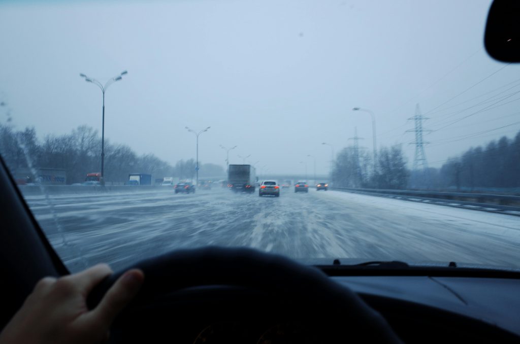View from a car driving on icy roads during winter twilight, showcasing traffic and snowy conditions.